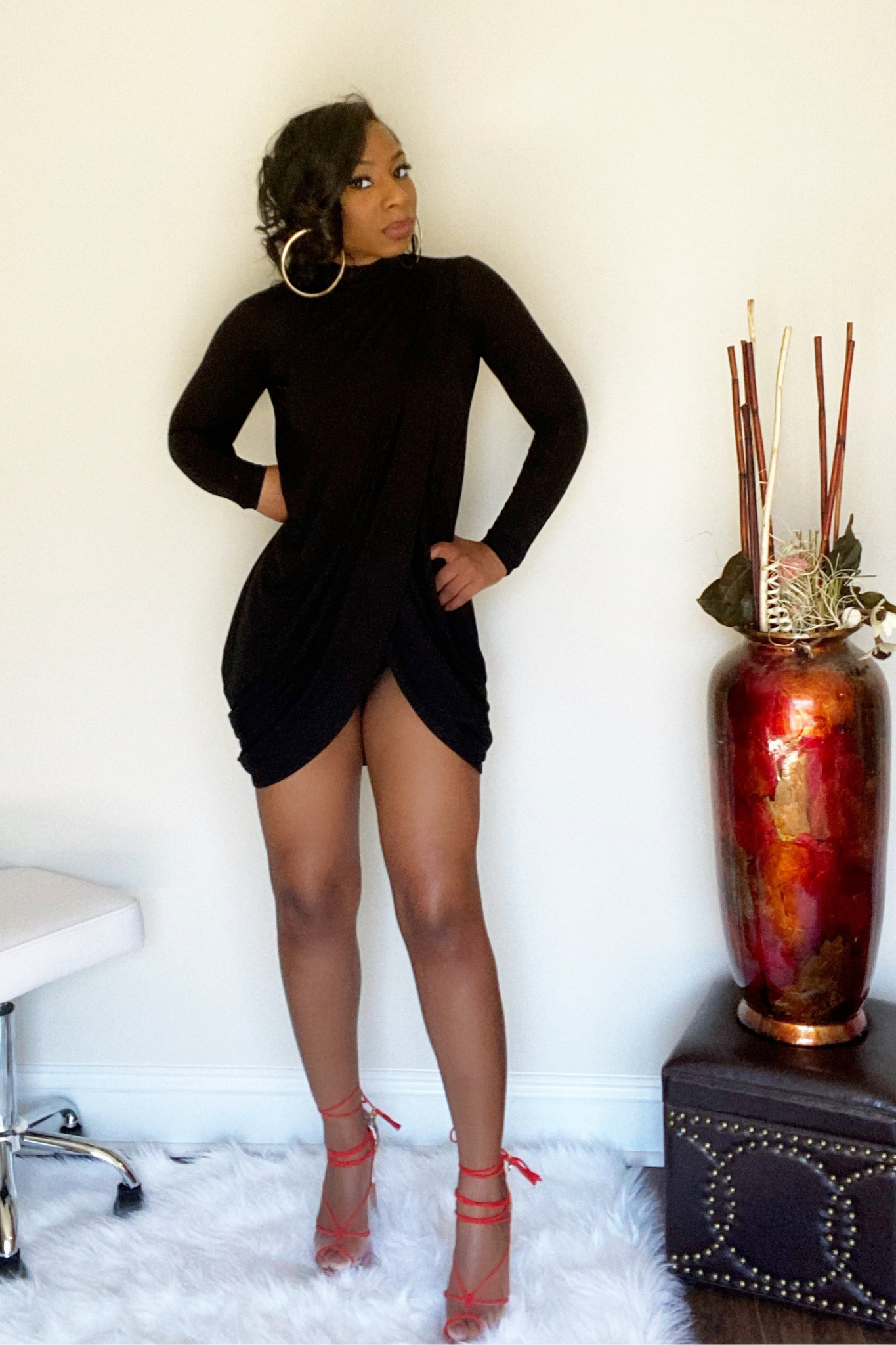 Front view of the long sleeve black mini dress. The top portion of the dress has draping down the middle that leads to a split in the upper thigh area.