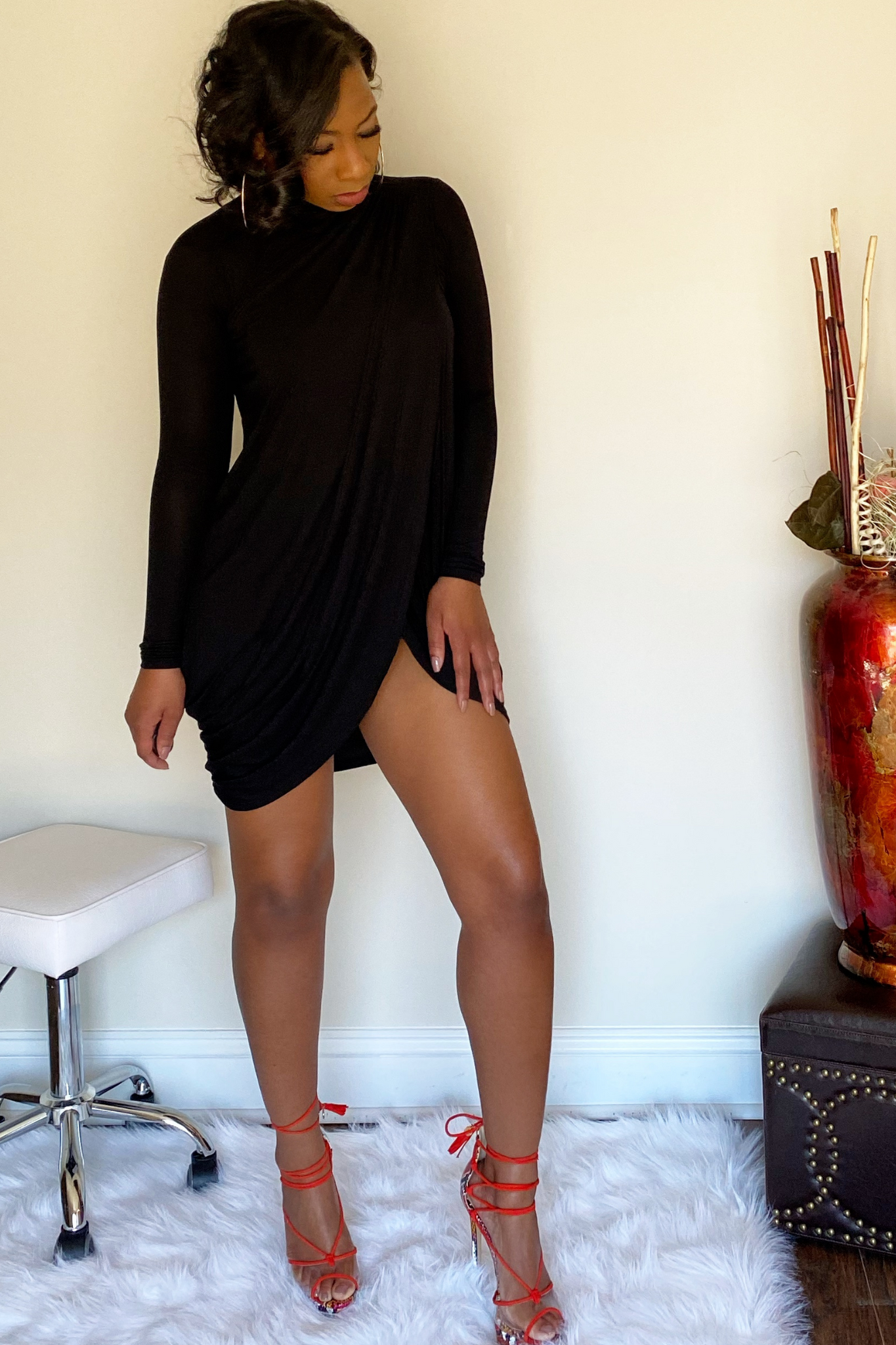 Front view of the long sleeve black mini dress. The top portion of the dress has draping down the middle that leads to a split in the upper thigh area.