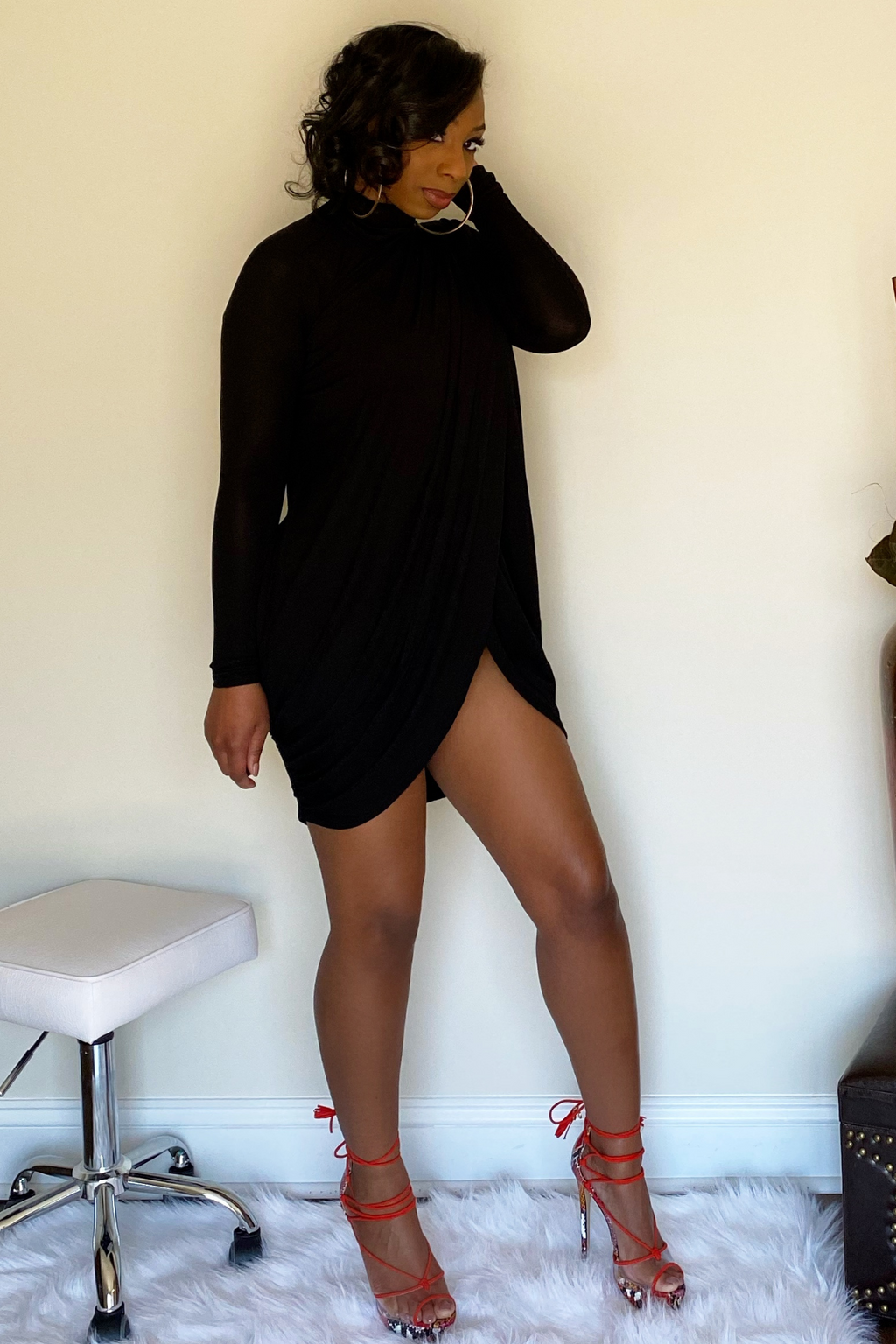 Side view of the mini black dress. Dress has long sleeves and stops mid-thigh with a split in the middle. The sides of dress have some rouching around the sides of the dress.