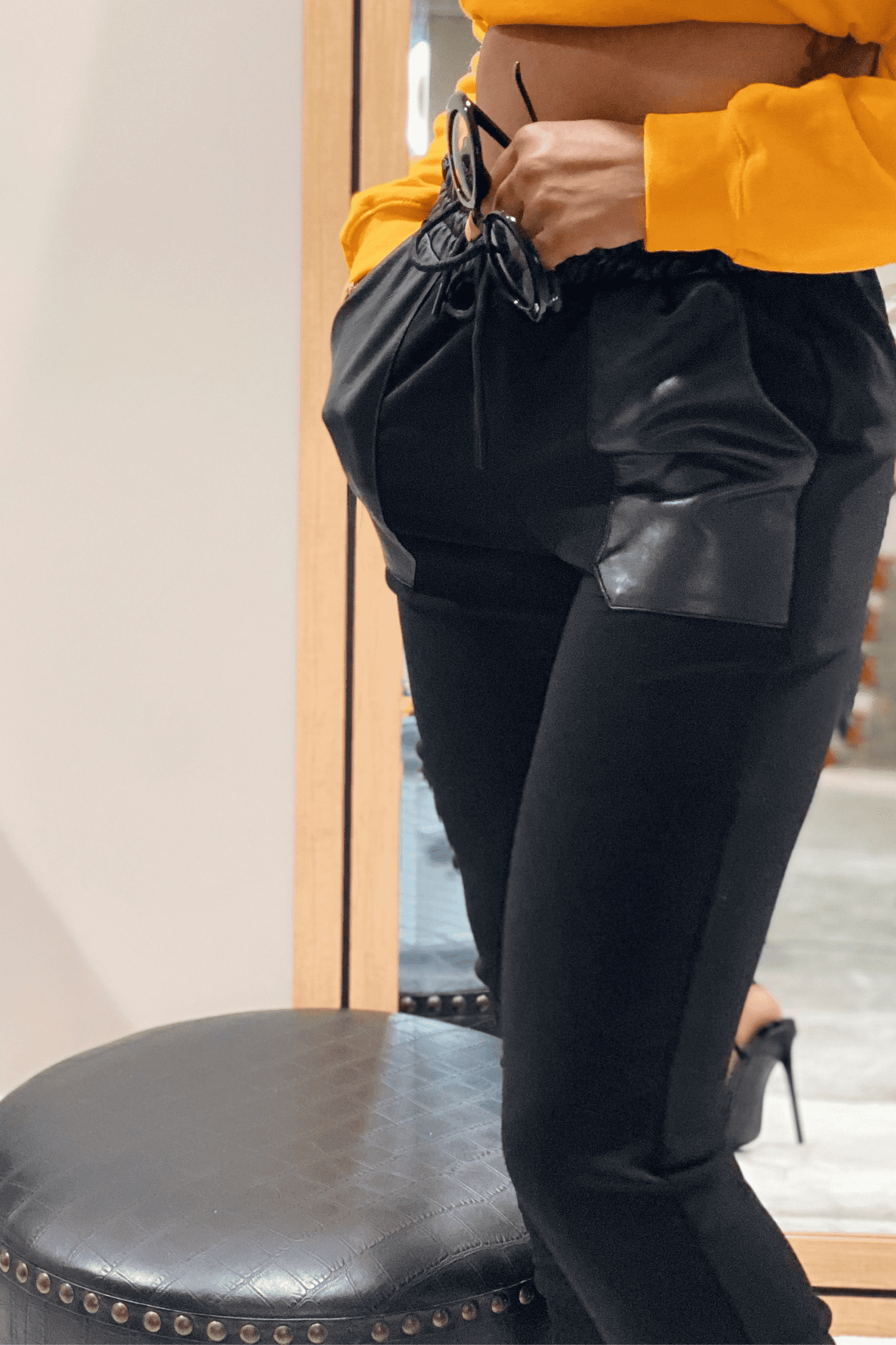 Close up side view of black joggers. The joggers have large faux leather pockets on the right and left sides, with faux leather waist band with adjustable drawstring in the front.