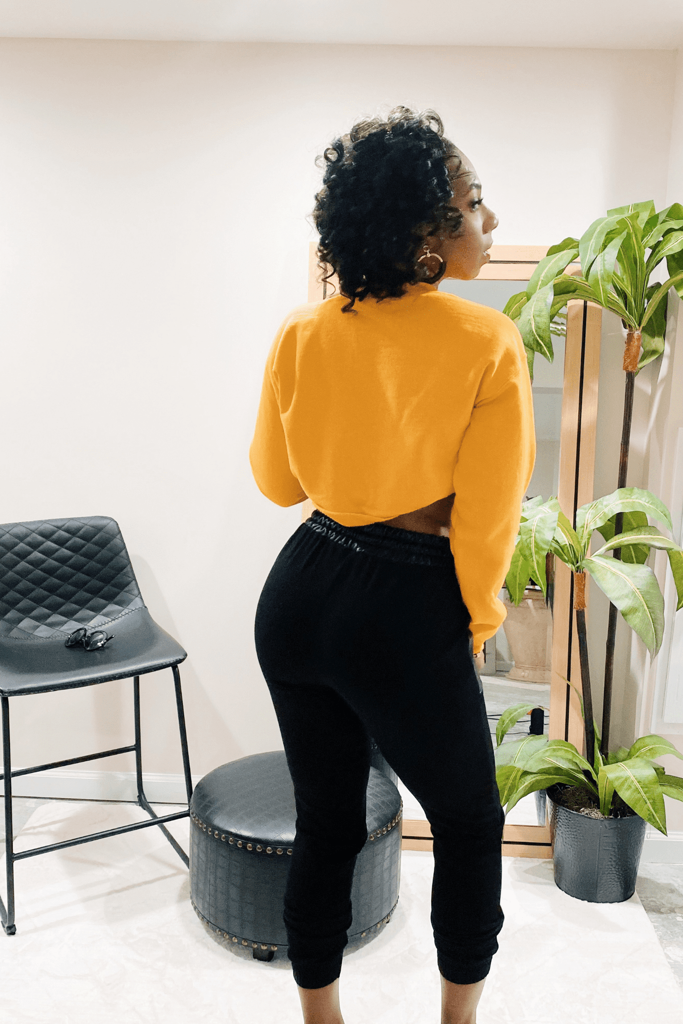 Back view of the black joggers. The Joggers have a black faux leather waistband. The joggers have no pockets in the back. The joggers are paired with a yellow cropped crewneck sweatshirt.