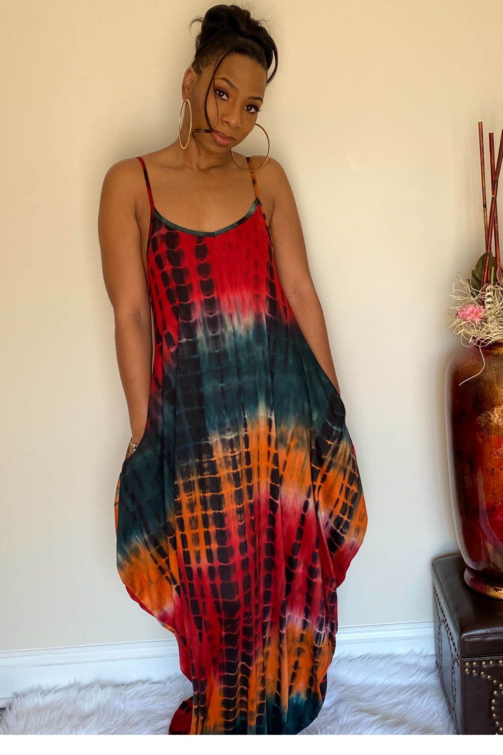 Front view of the tie dye maxi dress. The dress has a deep red, mustard yellow, black and dark green tie dye mix with adjustable spaghetti straps. The dress is maxi style that is fitted towards the top and slightly widens as it goes down. The dress has sleek hidden pocket on right and left side.