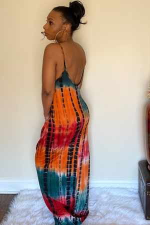 Back view of the tie dye maxi dress. The dress has a deep red, mustard yellow, black and dark green tie dye mix with adjustable spaghetti straps. The dress is maxi style that is fitted towards the top and slightly widens as it goes down. The dress has sleek hidden pocket on right and left side.