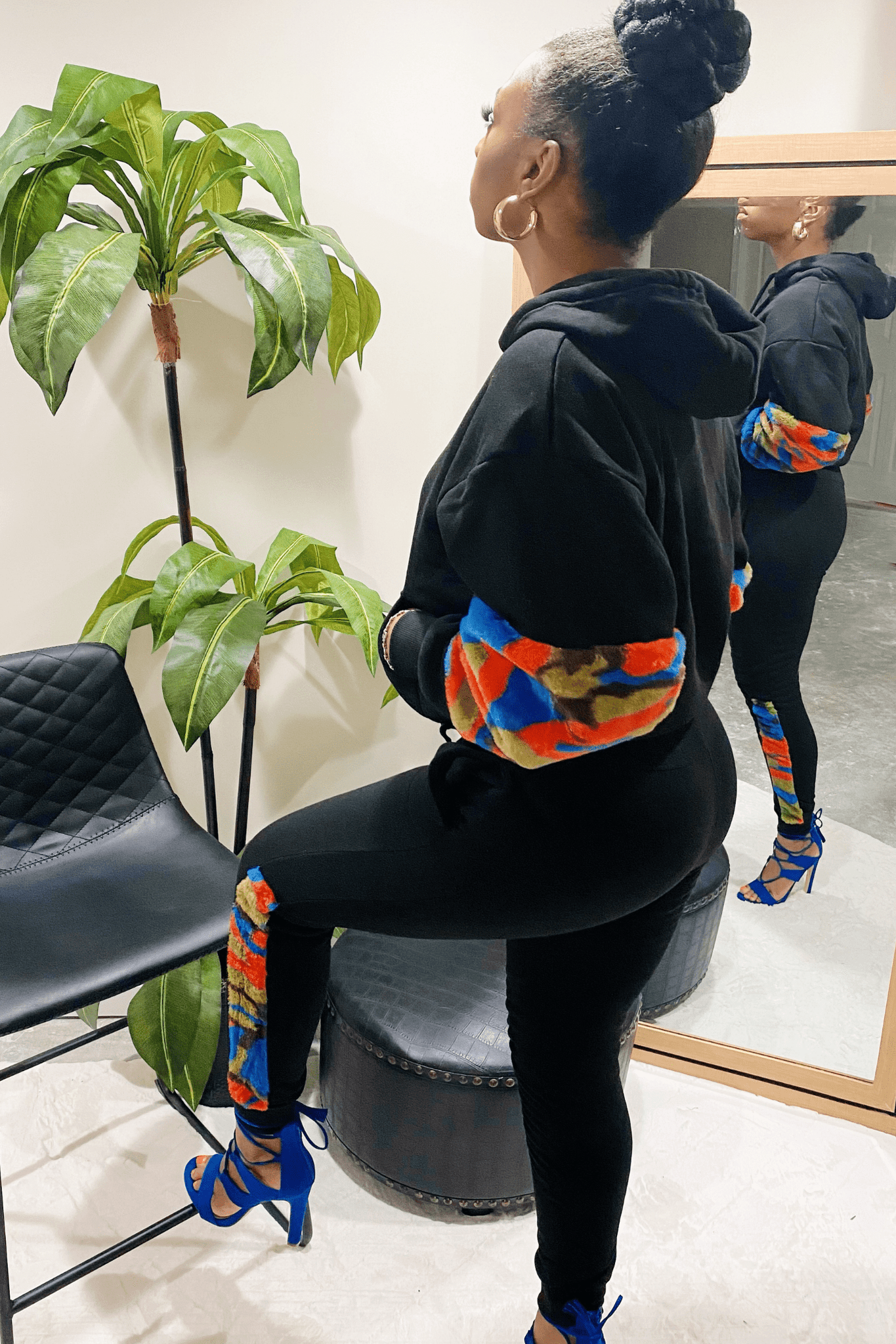 Side view of the black sweatsuit. The sweatsuit has a long sleeve hoodie top with a red, blue and green soft faux material that goes from the elbow to the wrist. The Jogger style pants are black with the same soft multicolored material going down the side of the leg from knee to the ankle.