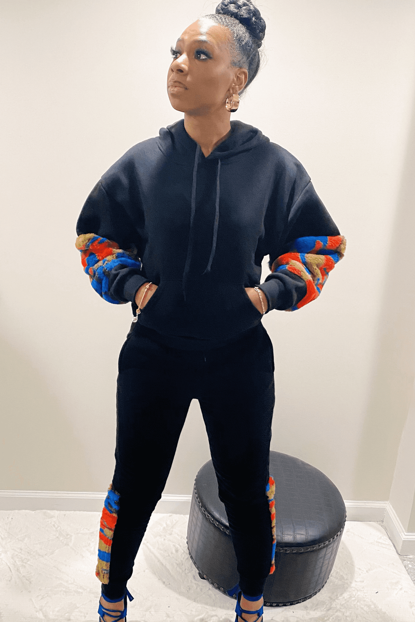 Front view of the black sweatsuit. The sweatsuit has a long sleeve hoodie top with a red, blue and green soft faux material that goes from the elbow to the wrist. The Jogger style pants are black with the same soft multicolored material going down the side of the leg from knee to the ankle.